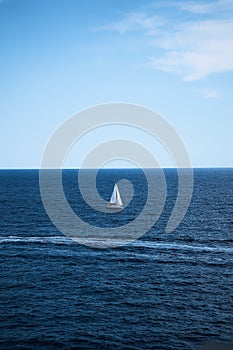 a lone white sailboat surrounded by deep blue water and a clear blue sky