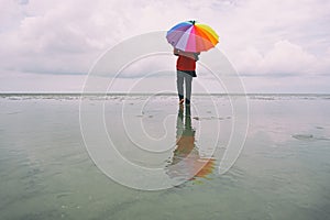 Lone woman at the beach with colorful umbrella