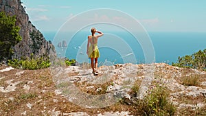 A lone woman hiker takes in the expansive view of Capri islands with rocky coastline and the Tyrrhenian Sea, dotted with