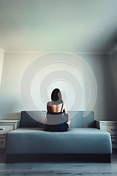 Loneliness. Alienation. Girl in an empty room sits back on a couch and looks in the wall photo