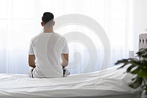 Loneliness Concept. Rear View Of Man Sitting On Bed In The Morning