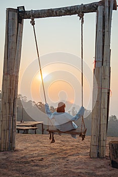 Loneliness woman sitting on the swing and looking at the sun at sunrise time