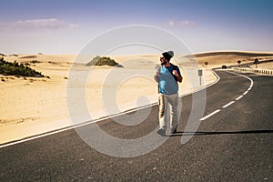 Lonely adventure traveler walk in the middle of the long scenic road with backpack - wanderlust travel lifestyle for adult people