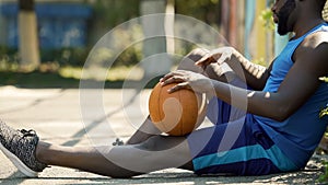 Lonely Afro-American basketball player sitting on ground with ball, sadness