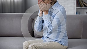 Lonely aging lady on sofa covering face, overwhelming problems, bad news