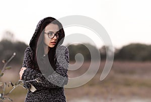 Lonely alone beautiful girl in warm sweater with hood looking aside in autumn field background. Picture of pretty depressed sad un