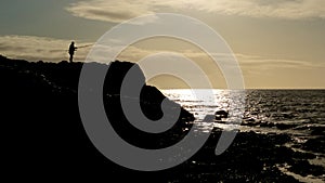 A lonely angler fishes from a coastal rock at dusk