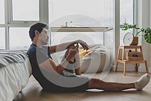 Lonely asian man using smartphone for social media alone in his apartment