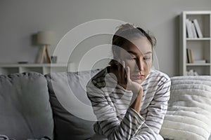 Lonely Asian woman in distress, worried, confused, sitting on sofa at home
