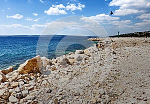 Lonely beach of coarse gravel on the coast of Dalmatia, Croatia with the shilouette of a griffin bird in the cloudy sky