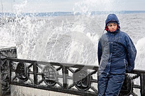 Lonely beatyfull girl in icy splashes of storm waves on the riverside with metal embankment