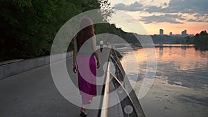 Lonely beautiful brunette girl walking on park embankment at sunset. Slow motion shot