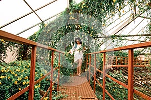 A lonely beautiful girl with multi-colored dreadlocks in a white dress stands on a red stairs in an arch of flowers. Greenhouse