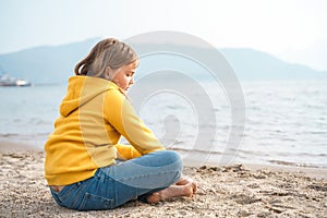 Lonely beautiful sad girl teenager sits thoughtfully on sand sea beach. Dreams,anxiety,worries about future,school