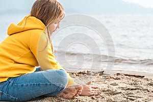 Lonely beautiful sad girl teenager sits thoughtfully on sand sea beach. Dreams,anxiety,worries about future,school