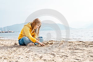 Lonely beautiful sad girl teenager sits thoughtfully on sand sea beach. Dreams,anxiety,worries about future,school