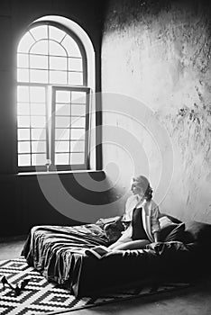 Lonely beautiful woman in the bedroom with large windows on the bed with a glass of wine relaxes. Black and white art photo in a