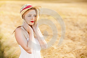 Lonely beautiful young blonde girl in white dress with straw hat