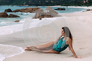 A lonely beautiful young girl lies on the shore of a white beach with large rocky stones, admires the sea surf, looks