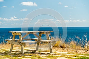 A lonely bench with a table on the edge of a cliff by the sea. Summer sun