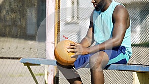 Lonely black man sitting alone on bench, playing ball and thinking about friends