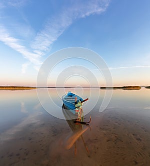 Lonely boat in calm lake. The silhouette is reflecting on the water. Beautiful summer day. Amazing sunrise. Blue sky with clouds.