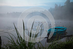 Lonely boat on a peaceful lake. Foggy autumn sunrise twilight. Bright blue turquoise shallop quiet forest, swamp plants