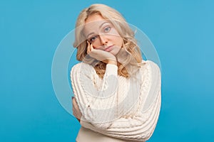 Lonely bored woman with curly blond hair looking at camera with disinterest leaning head on hand, depression, procrastination