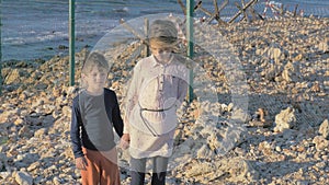 Lonely boy and girl immigrants wait at the border to continue their journey. High fence barbed wire on the rocky shore