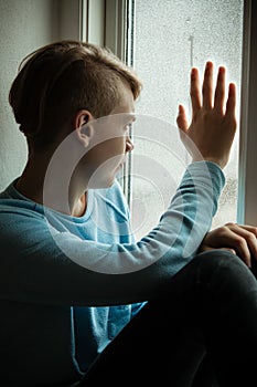 Lonely boy looking out of window