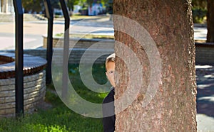 Lonely boy peeks out from behind a tree in an empty park