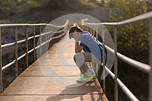 Lonely boy sitting on a suspension bridge