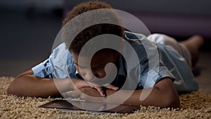Lonely boy watching tablet movie lying on floor at home, lack of communication