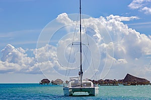 Lonely catamaran against the background on overwater bungalows stretching out across the lagoon in Bora Bora island