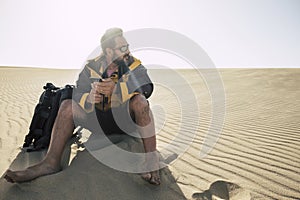 Lonely caucasian middle age man travel barefoot in the desrt with backpack and phone and tripod to take pictures. alternative