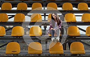 Lonely cheerleader girl sitting in stands and smiles sweetly.