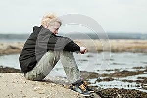 Lonely child with arms around knees outside