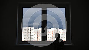 A lonely child looks out the window of his house in an apartment.