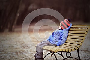 Lonely child sitting on bench in winter park