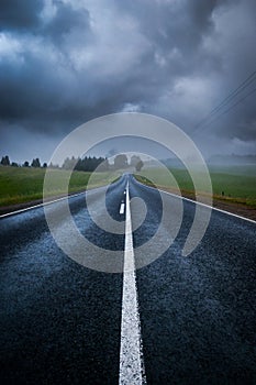 A lonely country road shrouded in mysterious moody clouds and mist