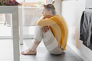 lonely depressed and sick woman sitting alone on kitchen floor in stress , depression and sadness feeling miserable in