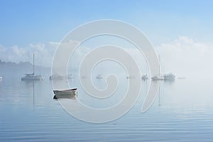 Lonely dinghy in foggy harbor