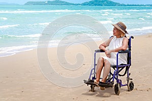 Lonely disabled senior elderly woman in wheelchair on tropical sand beach, Asian grandma looking at summer blue sea