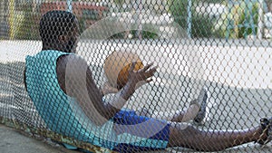 Lonely displeased man sitting at basketball court and holding ball, depression