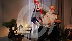 A lonely elderly disabled man wearing a T-shirt sits and waves a flag of Great Britain in his hand, in a wheelchair in