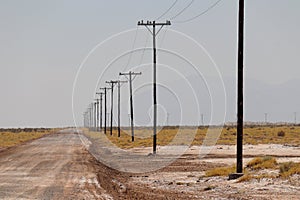 Lonely empty gravel road with poles stretching for miles into the desert