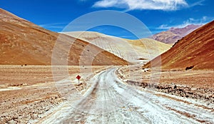 Lonely empty sandy road in hilly dry bare lonely valley between colorful desert hills, something lost curves ahead sign -