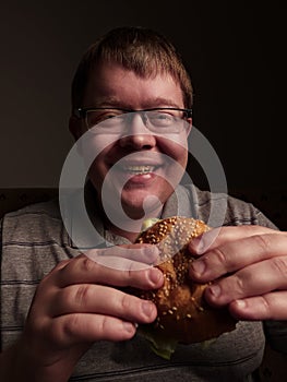 Lonely fat guy eating hamburger. Bad eating habits. Closeup.