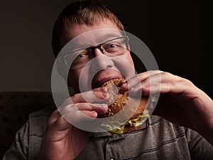 Lonely fat guy eating hamburger. Bad eating habits. Closeup.