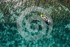 A lonely female in a straw hat smiling, relaxing lying floating in a kayak on the turquoise Adriatic Sea waves. Aerial coastal top